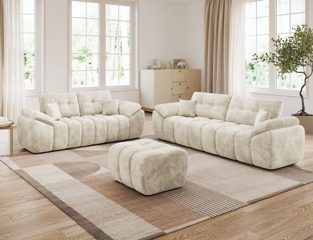 Helles Wohnzimmer mit zwei beigen Sofas und passendem Hocker auf Teppich vor großen Fenstern.