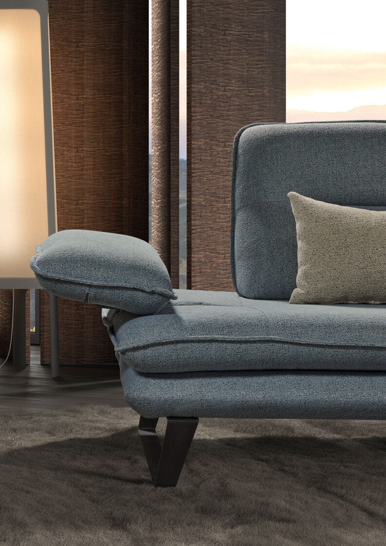 Detailaufnahme eines grauen Sofas mit Armlehne und Kissen vor Holzpaneelen und Fensterfront.