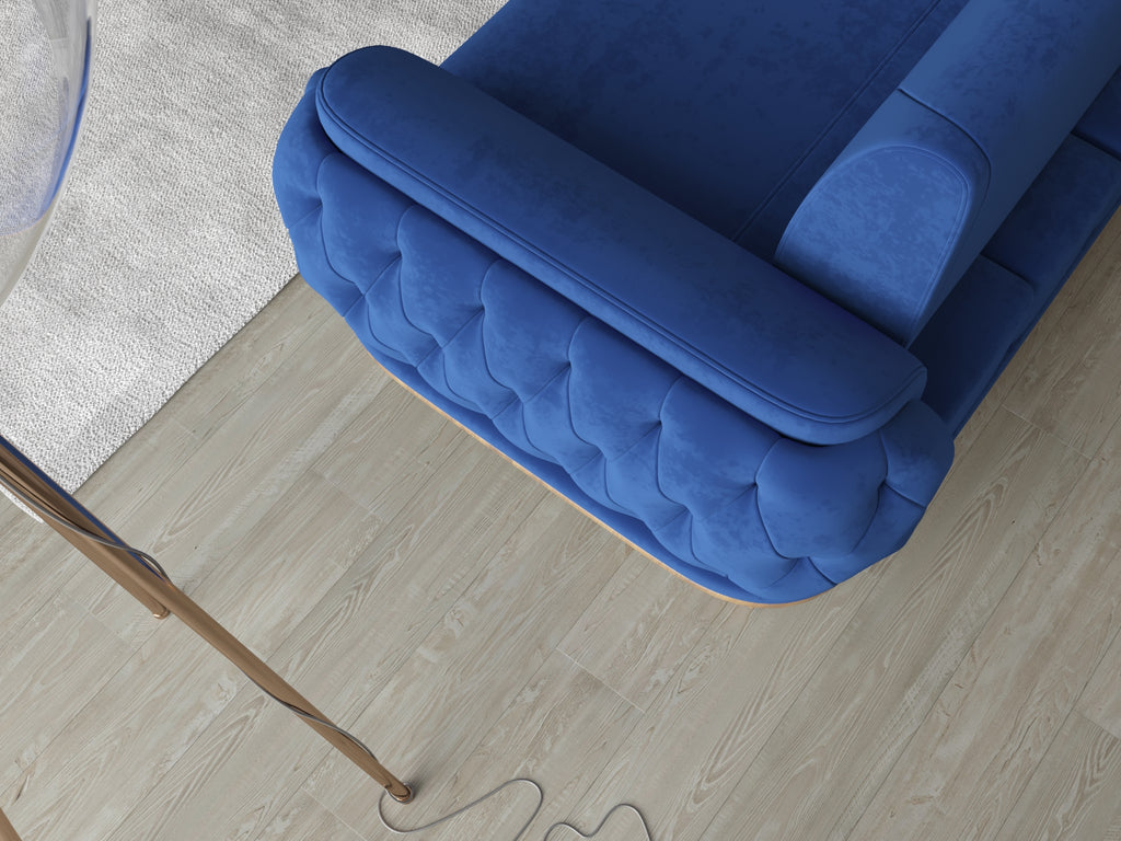 Draufsicht auf die Armlehne eines blauen Sofas mit gesteppter Polsterung auf hellem Holzboden.
