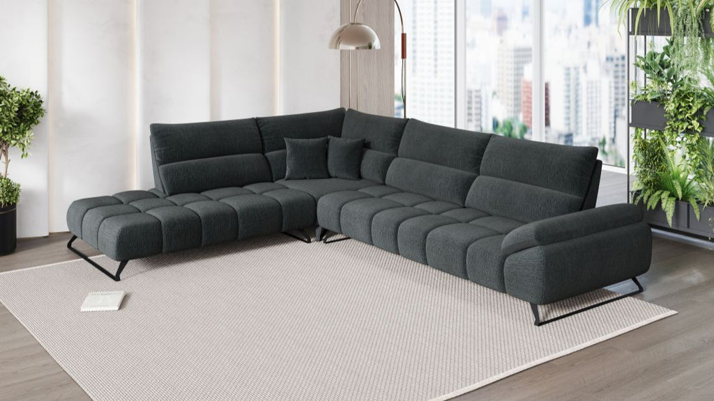 Großes dunkelgraues Ecksofa mit moderner Steppung in offenem Wohnraum mit großen Fenstern und Pflanzen.