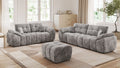 Helles Wohnzimmer mit zwei grauen Sofas und passendem Hocker auf Teppich vor großen Fenstern.