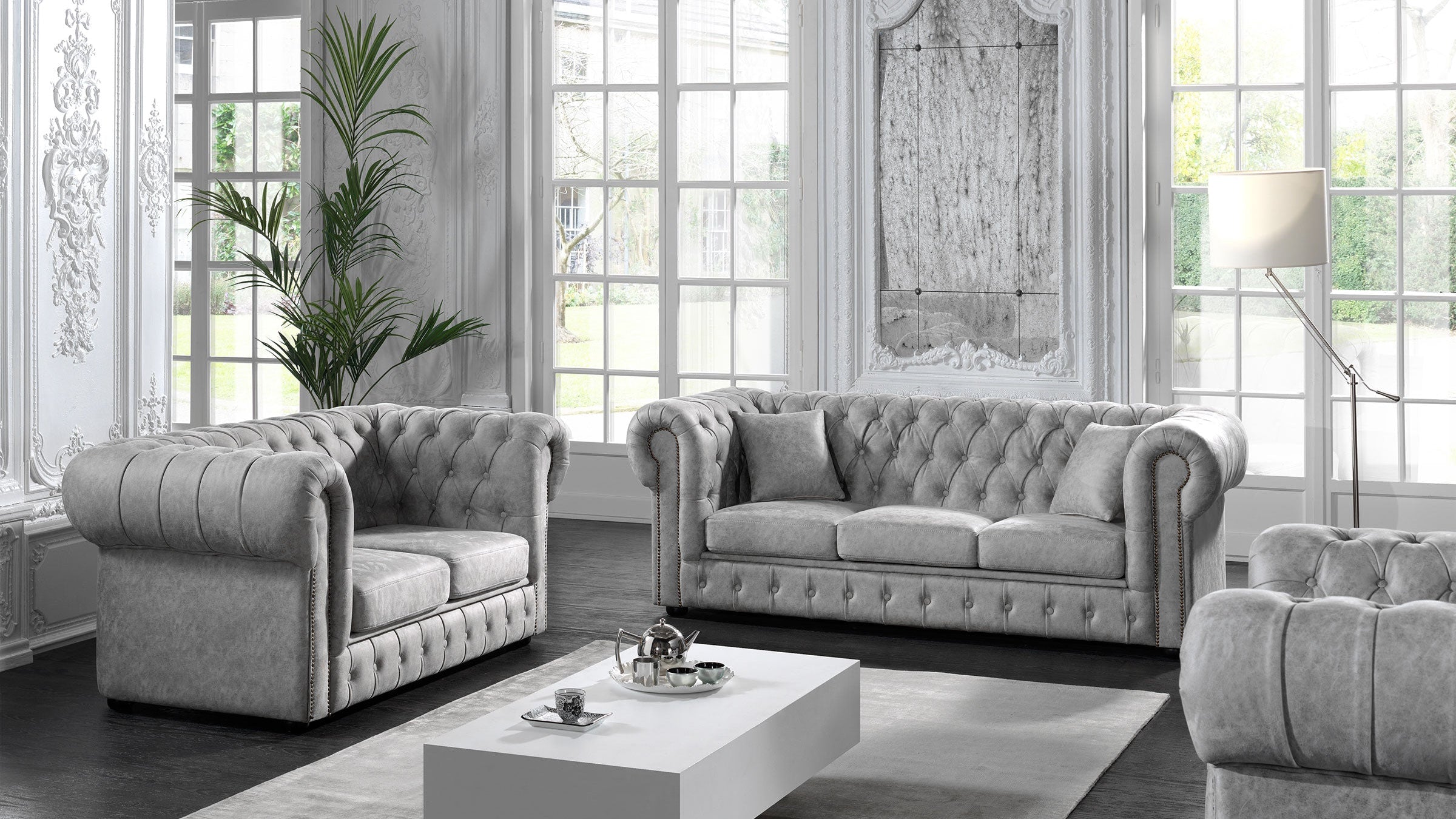 Graues Chesterfield Sofa Set im klassischen Wohnzimmer mit großen Fenstern und eleganter Einrichtung