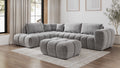 Graues modulares Ecksofa mit passendem Hocker in modernem Wohnzimmer mit großen Fenstern und hellen Vorhängen.