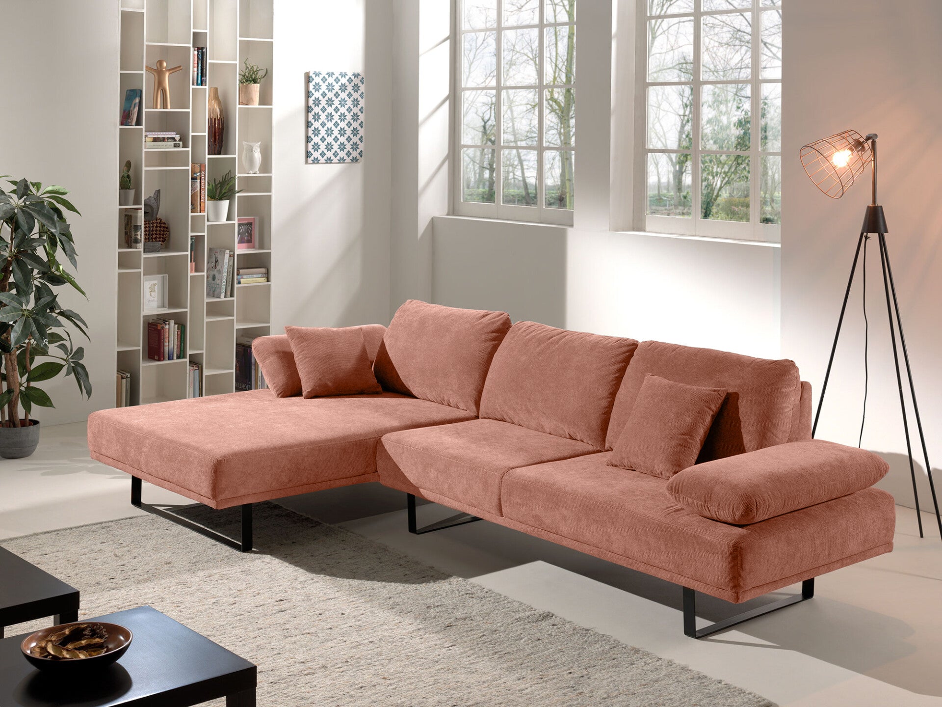 Modernes roséfarbenes Ecksofa mit Kissen in hellem Wohnzimmer mit Regal und Stehlampe