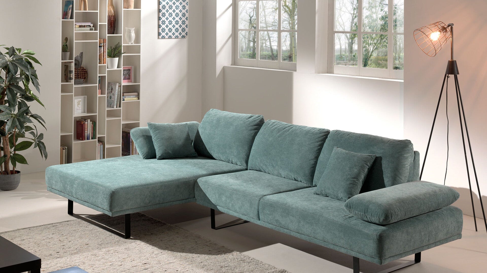 Modernes türkisfarbenes Ecksofa mit Kissen in hellem Wohnzimmer mit Regal und Stehlampe