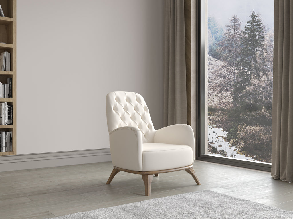 Cremefarbener Polstersessel mit Knopfheftung und Holzfüßen vor großer Fensterfront mit Blick auf winterliche Landschaft.