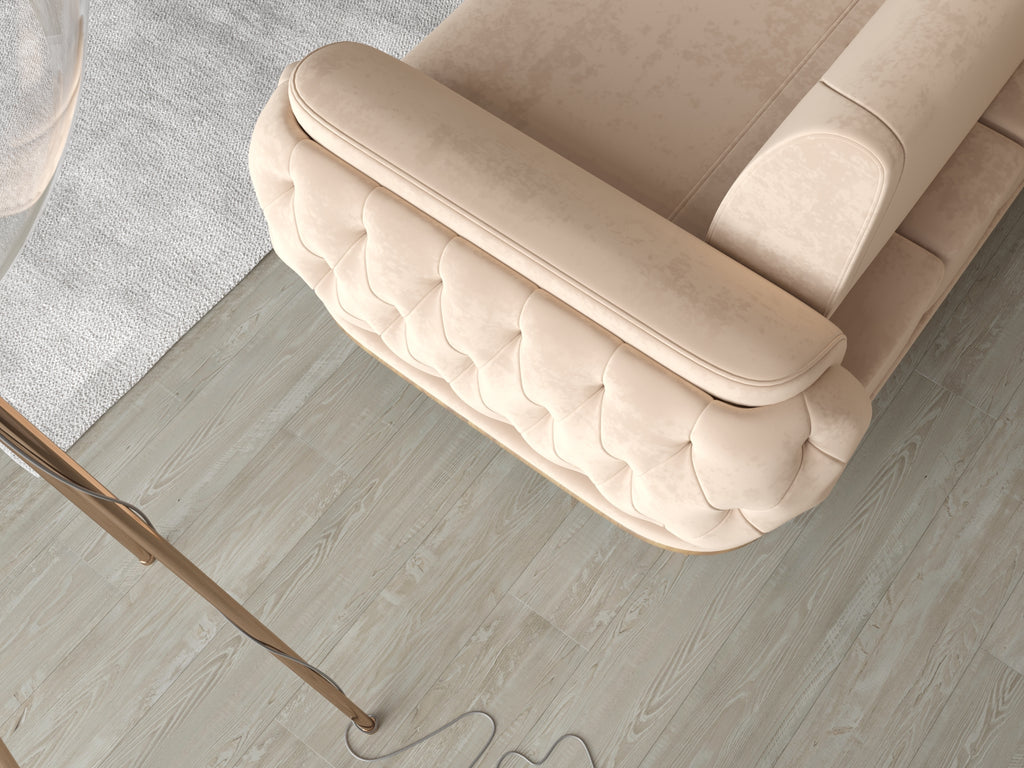 Beiges Sofa mit gepolsterter Knopfheftung in Draufsicht auf hellem Holzboden neben Teppich und Stehlampe.