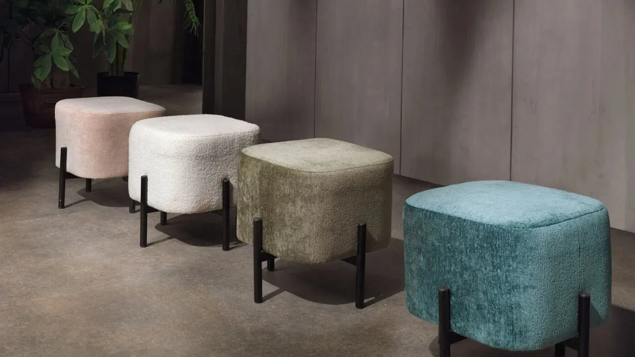 Vier gepolsterte Hocker in unterschiedlichen Farben mit schwarzen Metallbeinen